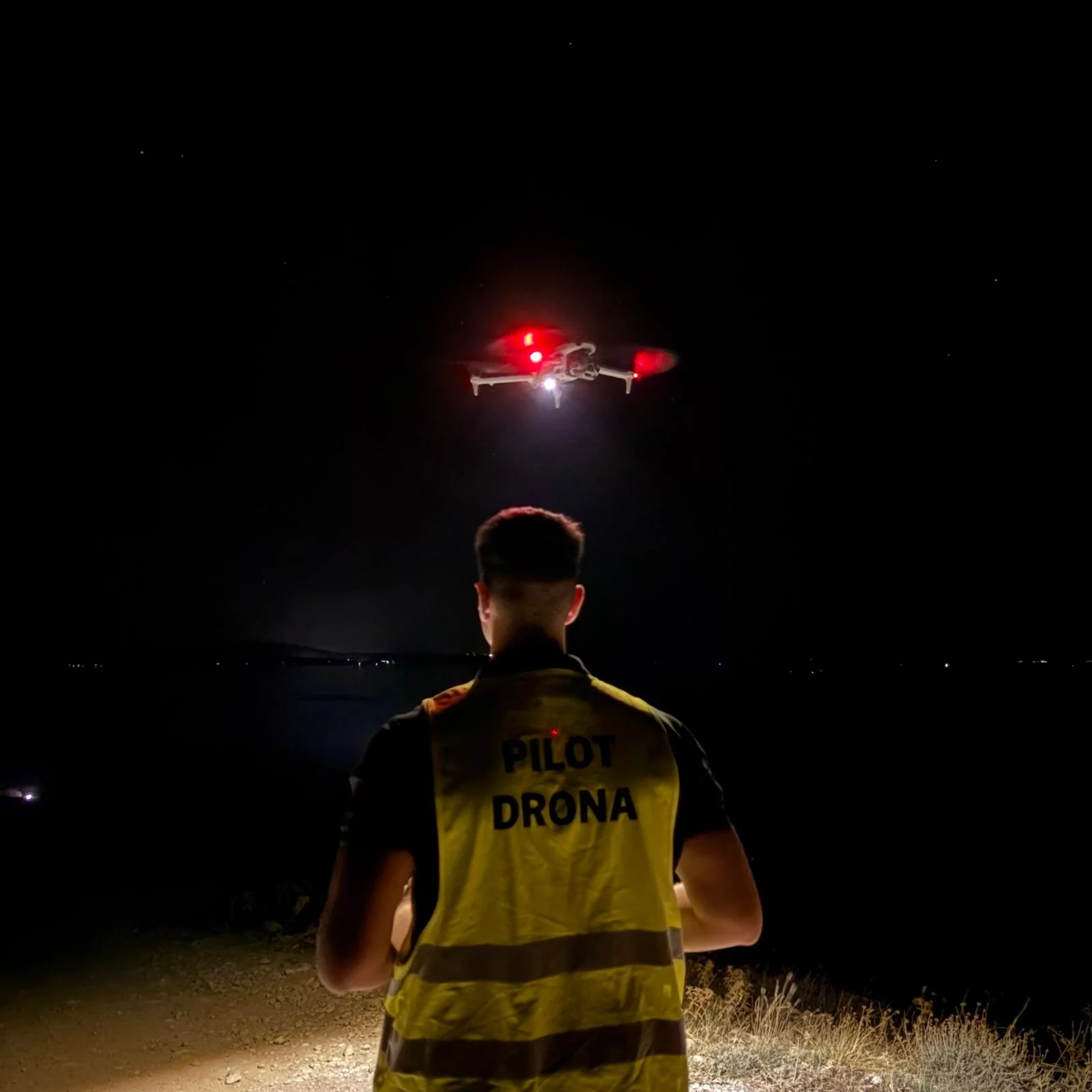 Pilot drona u reflektirajućem prsluku upravlja dronom tijekom noćnog leta